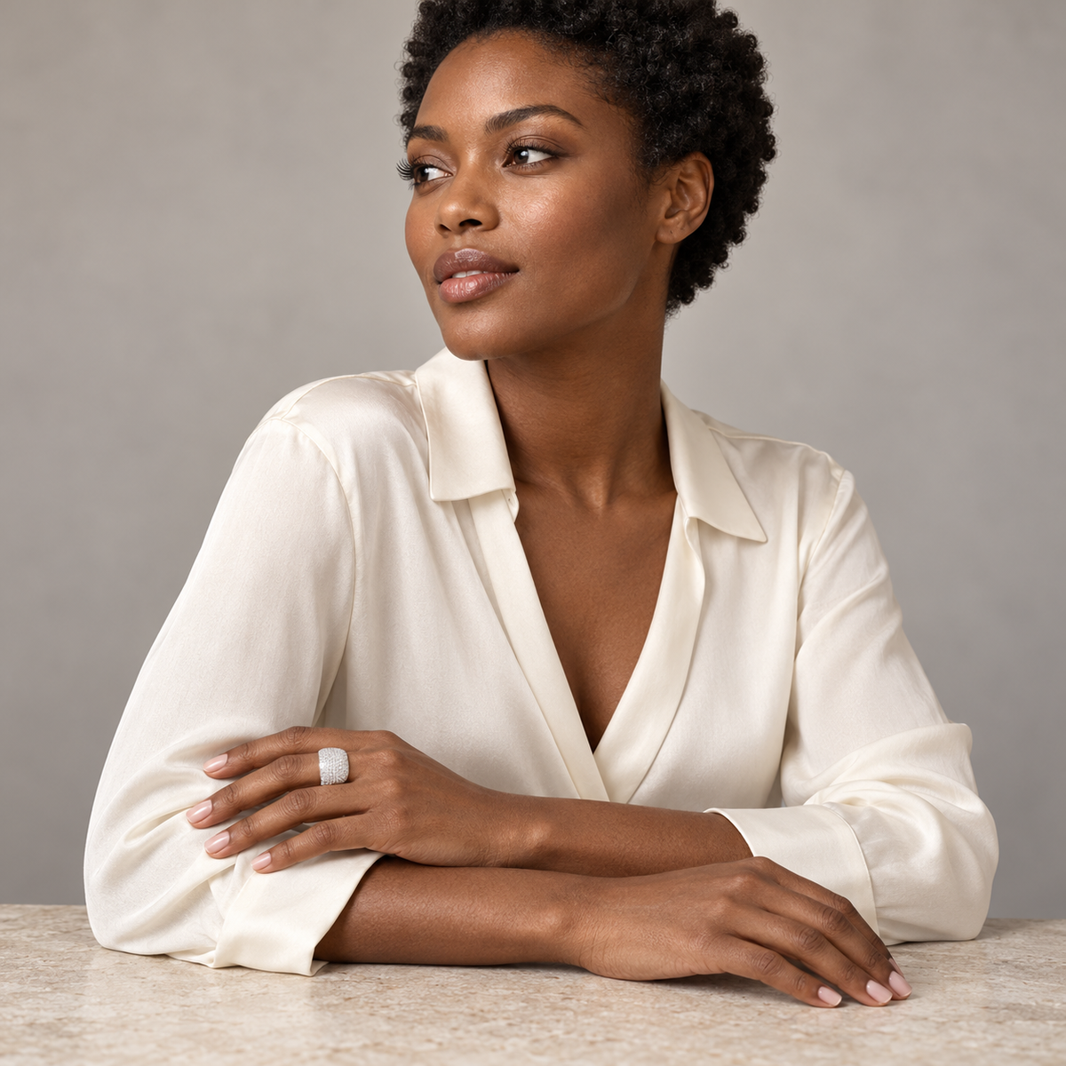 Model with short natural curls wearing the silver-tone Aurelia pavé dome ring, seated with her hands resting across her forearms at a studio table.